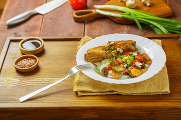 Thai chicken with rice and vegetables in a white plate on a wooden table next to soy sauce and vegetables in the background.