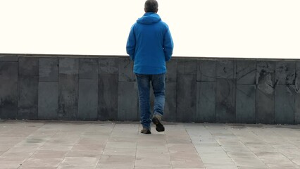 A lonely man in a blue coat walks and looks through the wall at the empty landscape