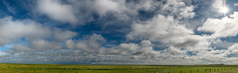 Panorama of dramatic summer puffy clouds in a blue sky above a flat green prairie landscape, Fences...