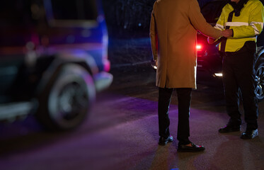 police officer stands next to a car he pulled over for speeding, reaching for the driver's ID, ...