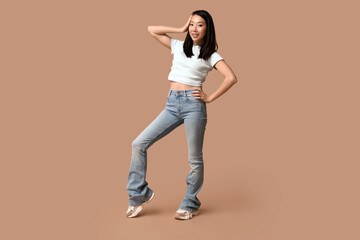 Fototapeta na wymiar Beautiful young happy Asian woman in stylish jeans on brown background