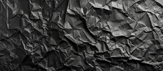 A closeup photo of a crumpled black piece of paper resembles the texture of bedrock. The monochrome photography captures the intricate pattern in shades of grey - obrazy, fototapety, plakaty
