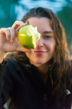 A vibrant snapshot captures a smiling skateboarder holding a bitten apple, taking a refreshing break on a city bridge