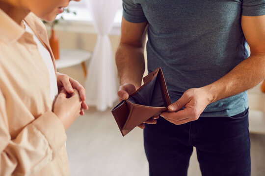 Close up shot of a poor family couple looking sadly at an open, empty wallet in husband hands, symbolizing financial problems and poverty. Concept of being broke and facing bankruptcy.