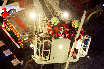 firefighters in firetruck crane  collecting pipes from a building in stormy day at night on city street - 770022451