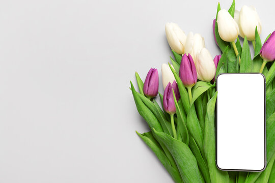 Composition with modern mobile phone and beautiful tulip flowers on grey background