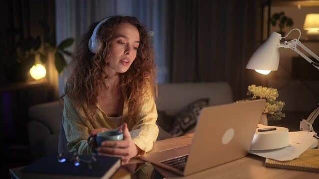 Focused young woman freelancer at night with cup of hot coffee for effective working at desk indoors Concentrated female with late work drinking caffeine for extra energy at home workplace Deadline