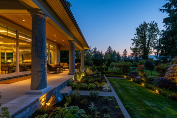 A sweeping twilight view of a luxurious residence, with inviting interior lights, an elegant porch featuring outdoor living spaces, and a meticulously cared-for garden.