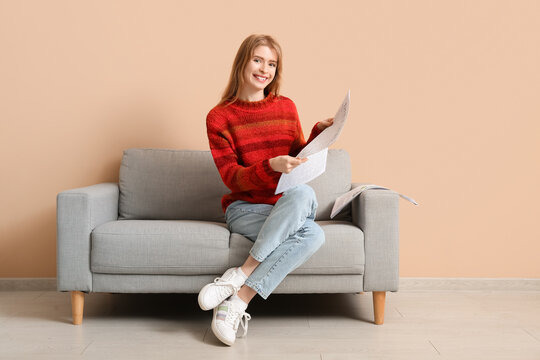 Happy young woman with newspaper sitting on sofa near color wall