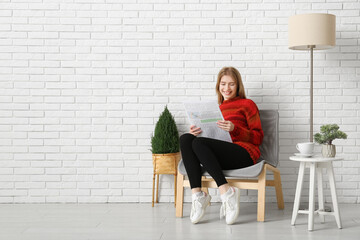 Young woman reading newspaper on chair at home