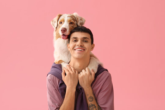 Young man with Australian Shepherd dog hugging on pink background