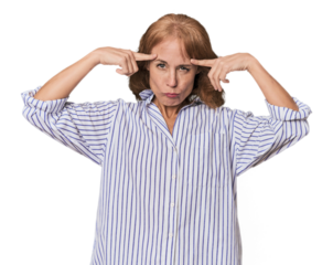 Redhead mid-aged Caucasian woman in studio focused on a task, keeping forefingers pointing head.