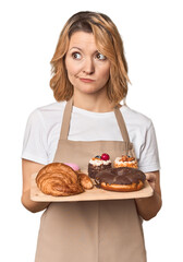 Middle-aged Caucasian woman baker with pastries confused, feels doubtful and unsure.