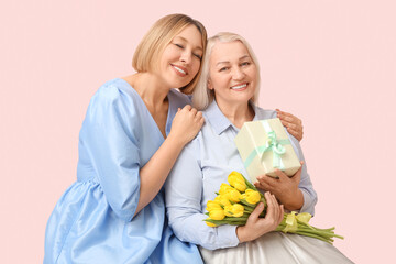 Adult woman with her smiling mother, gift box and bouquet of tulips on pink background....