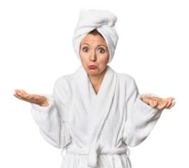 Caucasian woman in bathrobe and towel doubting and shrugging shoulders in questioning gesture.