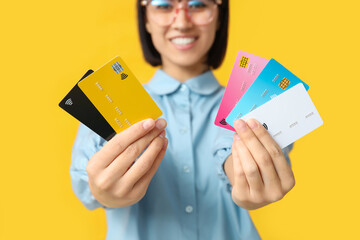 Beautiful young woman with many credit cards on yellow background