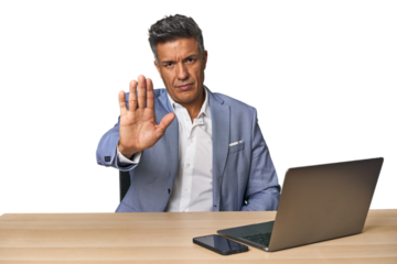 Elegant businessman at desk with laptop standing with outstretched hand showing stop sign, preventing you.