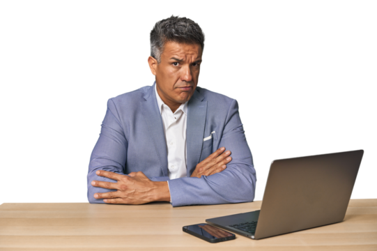 Elegant businessman at desk with laptop frowning face in displeasure, keeps arms folded. - Powered by Adobe