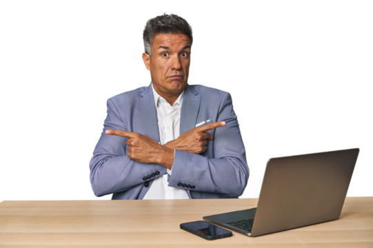 Elegant businessman at desk with laptop points sideways, is trying to choose between two options. - Powered by Adobe
