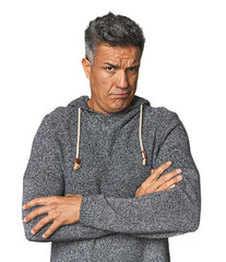 Middle-aged Latino man frowning face in displeasure, keeps arms folded.