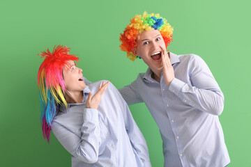 Business colleagues in funny wigs on green background. April Fools' Day celebration