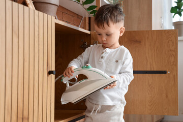 Little boy taking electric iron from drawer at home. Child in danger