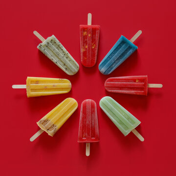 Colorful assortment of fruit popsicles on red. Generative AI image