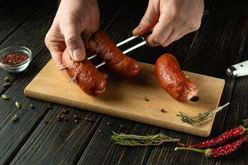 Preparing to cook a delicious grill with Munich sausages. A fork with sausages in the hands of a...