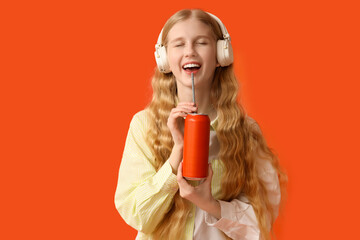 Beautiful young woman in headphones with can of soda on orange background