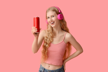 Happy young woman in headphones with can of soda on pink background