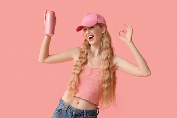 Beautiful young woman with can of soda showing ok gesture on pink background
