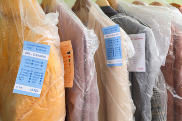 Rack with outwear in plastic bags after dry-cleaner's on green background, closeup