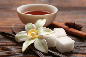 Fototapeta na wymiar Beautiful vanilla flower, sticks, extract and sugar on wooden background, closeup