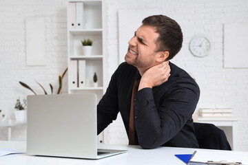 Businessman suffering from neck pain at table in office