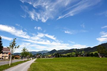 A picturesque view of a small village and a road with houses. In the background are distant mountains of mountains under a blue sky