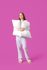 Young woman in pajamas with pillow on purple background