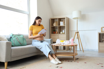Young pregnant woman with maternity hospital bag writing checklist on sofa at home
