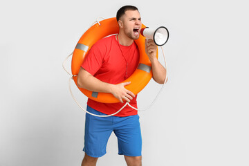 Young lifeguard with lifebuoy shouting into megaphone on white background
