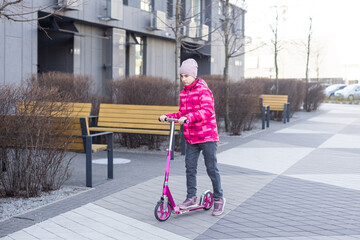 Little cute girl riding a scooter on a path in the park