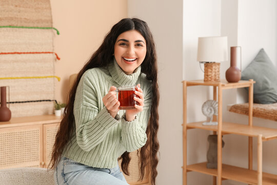 Happy young woman with glass cup of hot tea at home