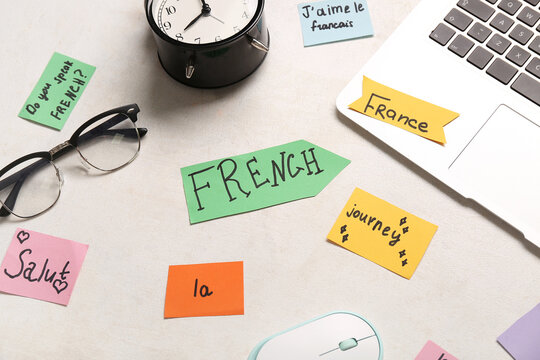 Composition with French words, modern laptop and eyeglasses on light background