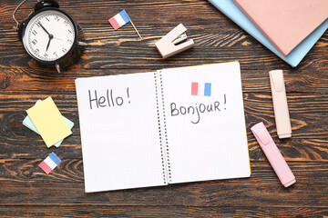 Notebook with text HELLO, BONJOUR, stationery and alarm clock on wooden background © Pixel-Shot