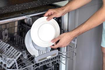 Close-up of male hands putting dirty ceramic dish in the dishwasher. Household and helpful...