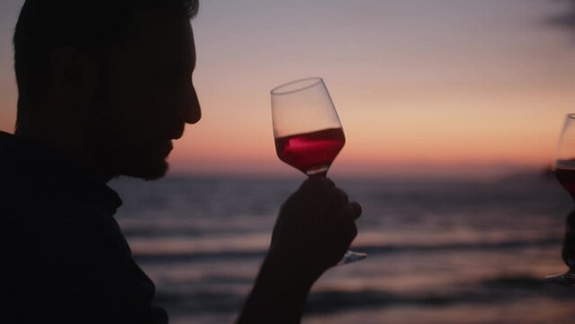 Multiethnic boyfriend and girlfriend drinking wine against beach sunset sky