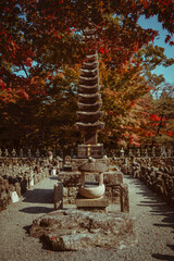 An ancient stone pagoda stands amidst rows of stone figures under a fiery autumn canopy.