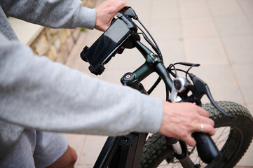 Close-up male hands on the handlebar of an electric bike in the city, smartphone with black mockup screen copy ad space