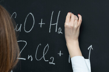 Back view of a female student writing the formula of a chemical reaction on the blackboard	