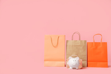 Shopping bags and piggy bank on pink background