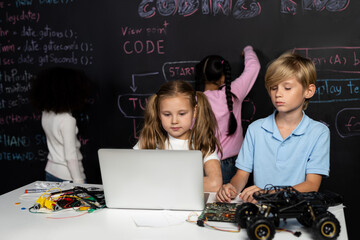 Smart girl in white bib learning about coding robotics technology using laptop in the STEM class....
