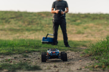 Focus on remote control car in nature with man in blurry background.